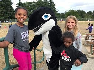 Three students stand together with a school mascot Orca
