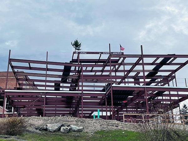 a structural steel framework has a top beam with a flag and an evergreen tree