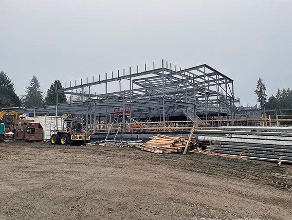 structural steel frame for large building with dirt, materials, and equipment in front