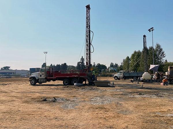 a drilling rig stands above a field of dirt covered in straw. trucks are in the photo