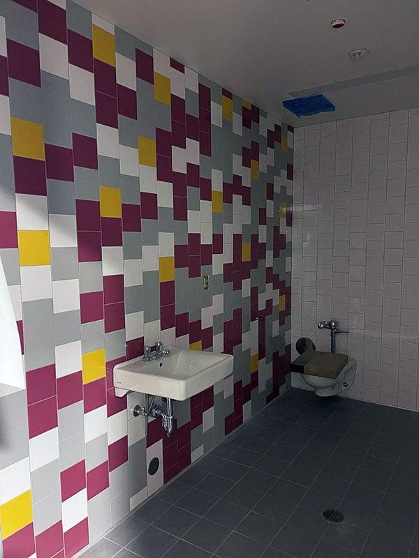 a purple, yellow, white, and gray tiled wall with a sink and a toilet