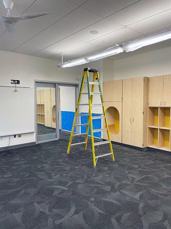 a large room has cabinets, carpet, and a ladder