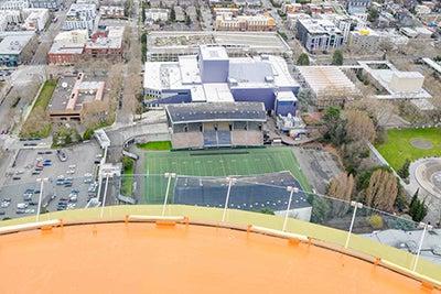 a curved orange surface in the foreground looks down to an athletic field and grandstands below with other buildings on the outside