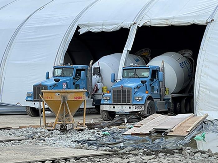 two cement mixer trucks are backed into openings in a large white tent