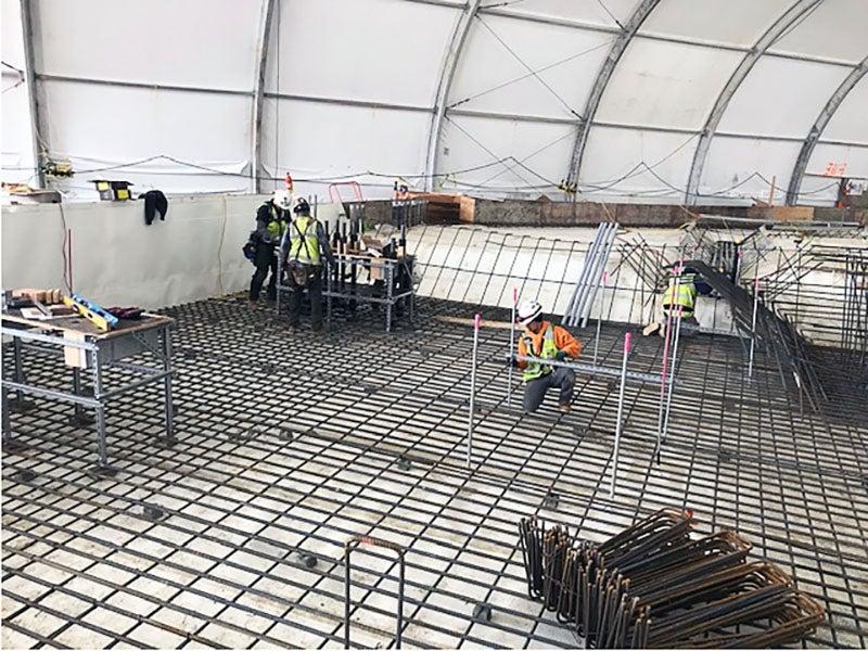 workers installing rebar in a pit under a big tent